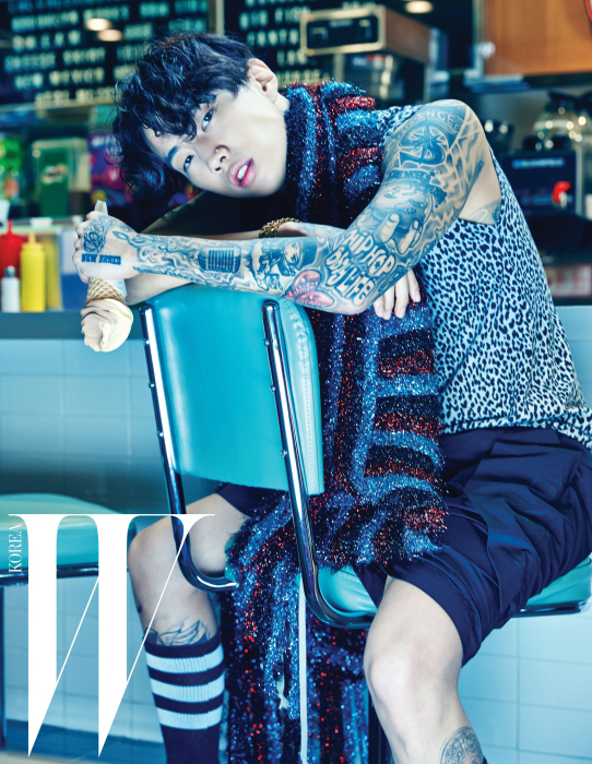 호피 무늬 슬리브리스 티셔츠는 Saint Laurent by Boon the Shop 제품. 반짝이는 니트 머플러는 Martin Margiela 제품. 팬츠는 Rick Owens 제품. 골드 워치는 Versace 제품.