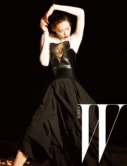 추상 작품이 연상되는 패턴이 그려진 하얀색 톱과 가죽 뷔스티에, 검은색 주름 스커트는 Loewe 제품.