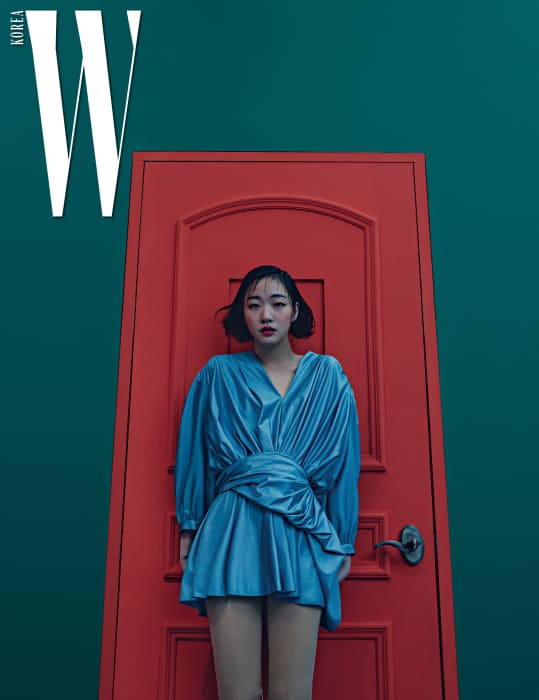 동그란 어깨 실루엣과 주름이 우아함을 더하는 푸른색 드레스, 스판덱스 소재의 팬츠 형태 부츠는 Balenciaga 제품.