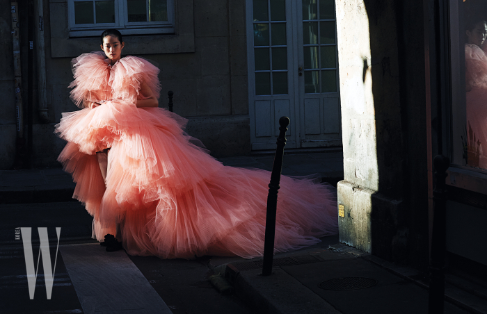 풍성한 샤가 겹겹이 층을 이룬 핑크색 드레스, 폼폼 장식 플랫 슈즈는 Giambattista Valli 제품.