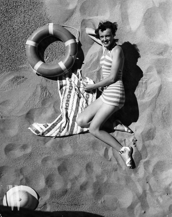 1935:  A surf girl relaxes on Palm Beach, Australia, beside a life-ring.  (Photo by Topical Press Agency/Getty Images)